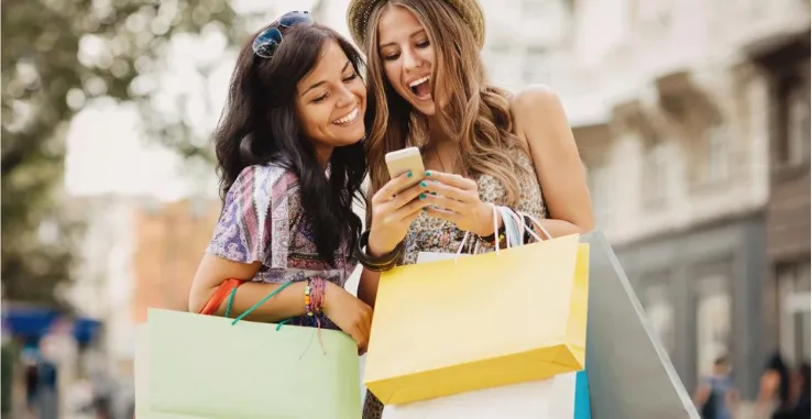 Two ladies on a shopping trip holding bags and looking at a phone smiling